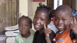 Three young African children smile as they wait in a detention centre.