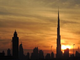 The Dubai skyline is silhouetted against the sunset with the Burj Khalifa prominent among the buildings.
