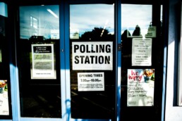 A sign for a polling station sits in a glass door.