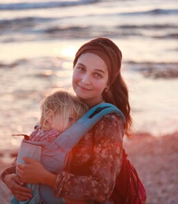 Young refugee woman and her child stand posing in front of a body of water at sunset.