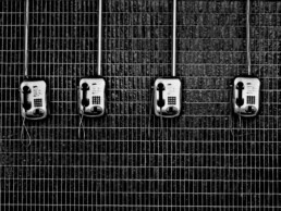Four black and white public phones hang on a tiled wall.