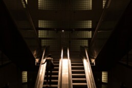 man stands on an escalator in a dimly lit foyer