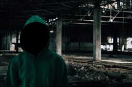 A mysterious hooded figure stands in front of an abandoned underpass