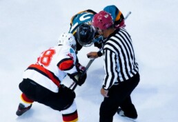 Hockey players face off on the ice as a referee prepares to drop the puck.