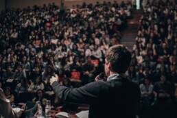 Man gives a speech in front of a large auditorium filled with people