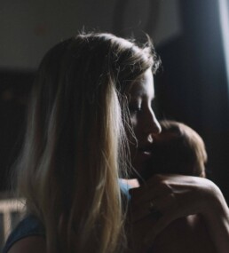 Mother holds her child in a dark room with a sliver of natural light shining through