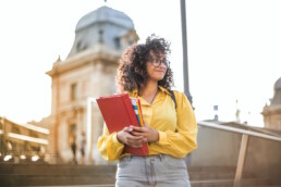 Woman with curly hair wearing yellow shirt holding school books